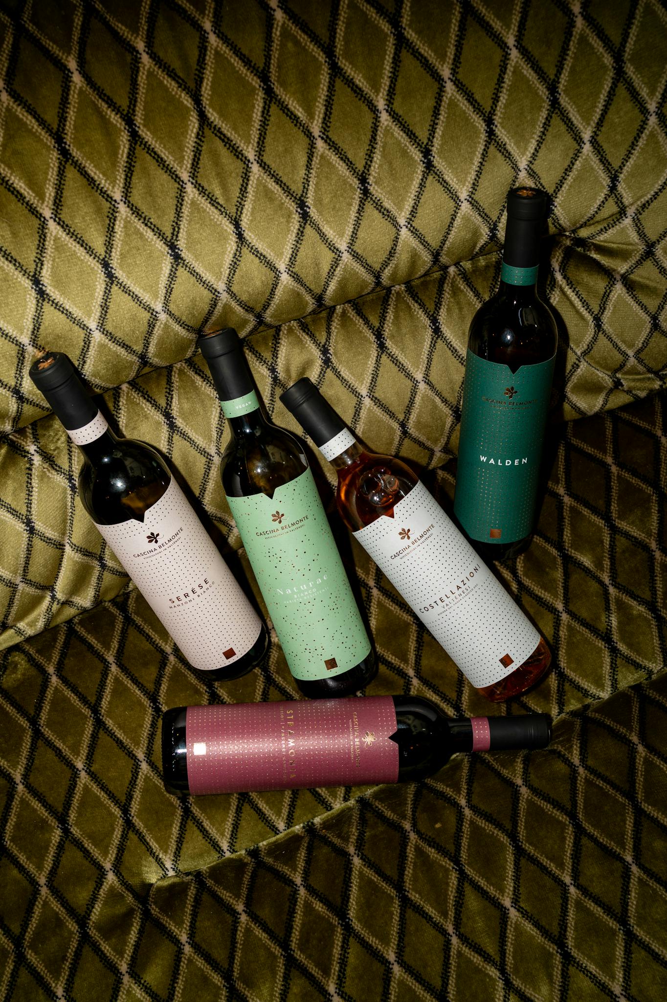 Collection of wine bottles displayed on a stylish carpeted sofa, showcasing elegant labels.